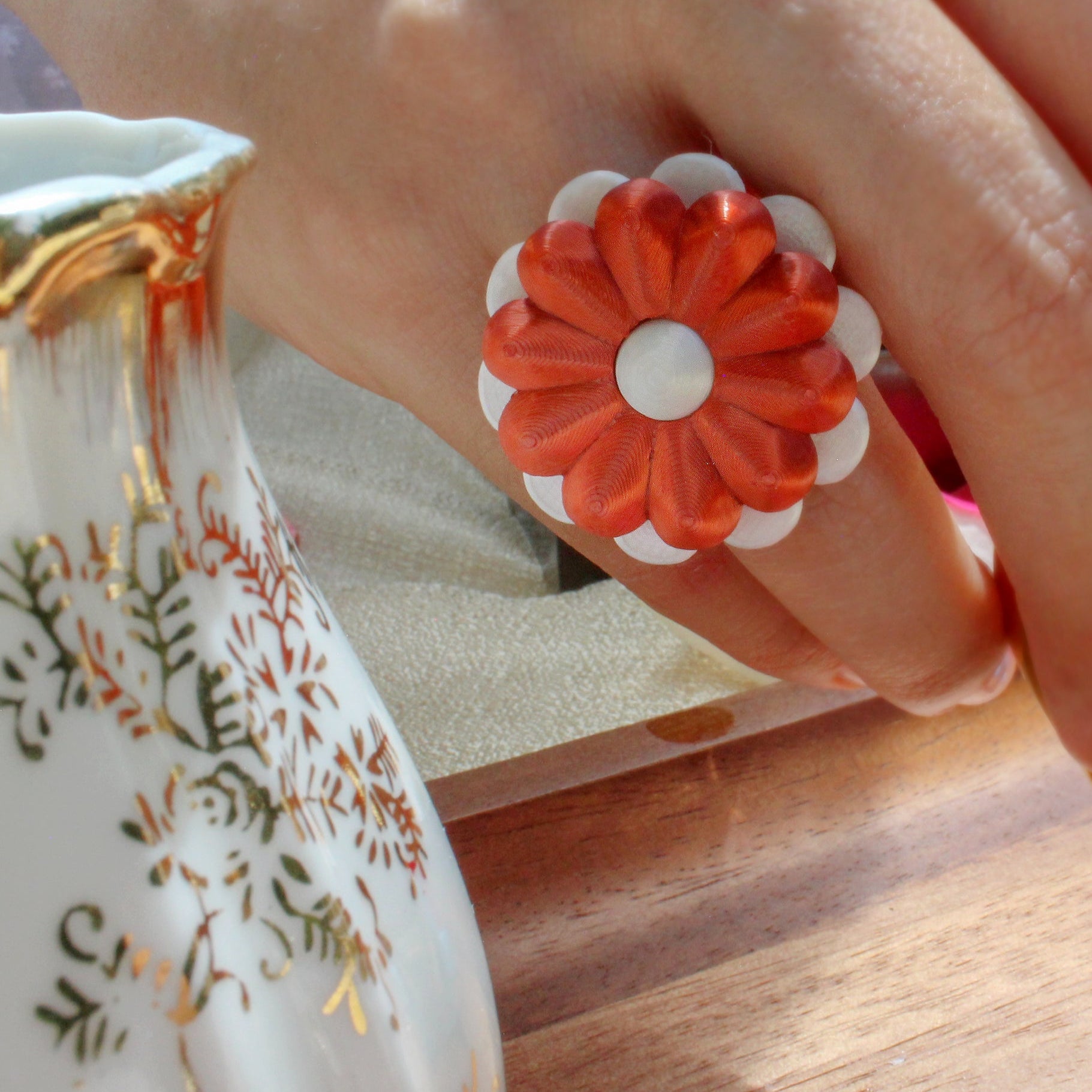 Hand wearing a floral ring with a decorative teacup and saucer in the background