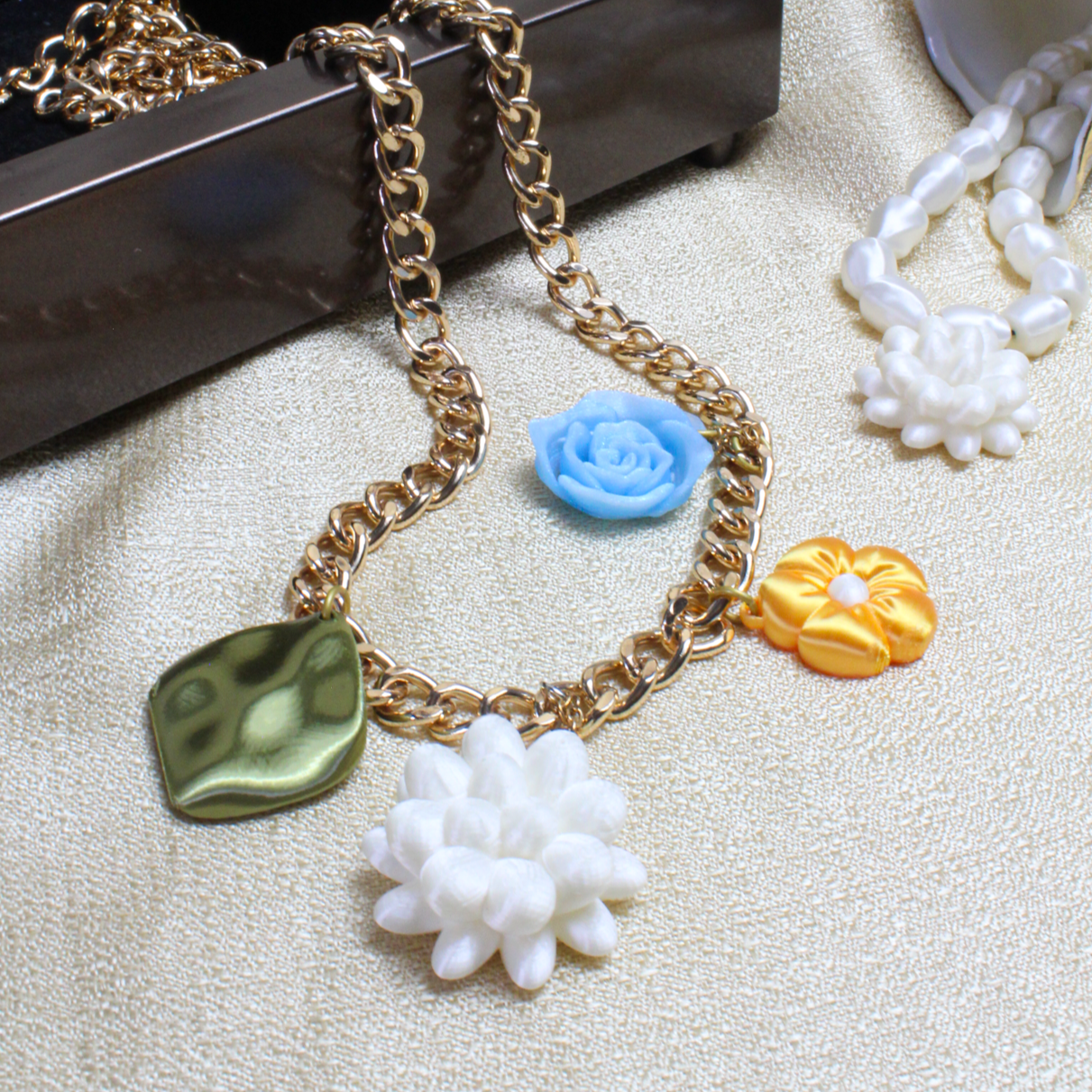 Necklace with floral charms on a textured surface with a box and glass in the background