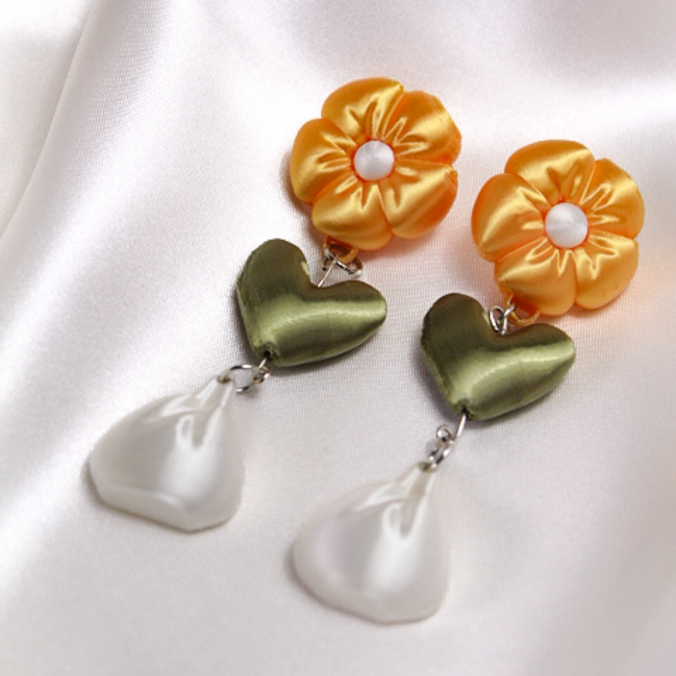 Pair of earrings with yellow flower and green heart design on a white background