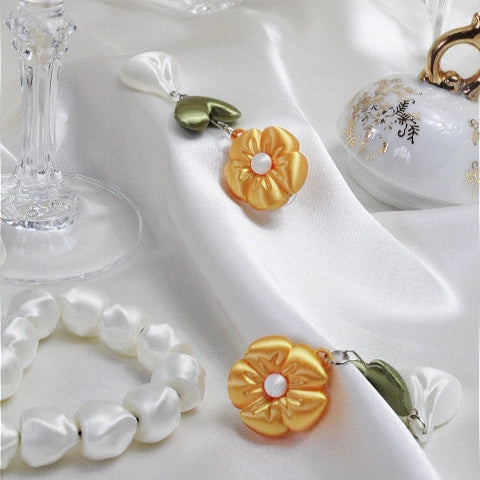 Gold flower-shaped earrings with pearl center on a white fabric background